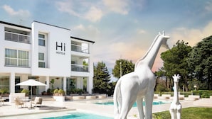 Un hotel moderno con piscina, mobiliario exterior y una estatua de jirafa.
