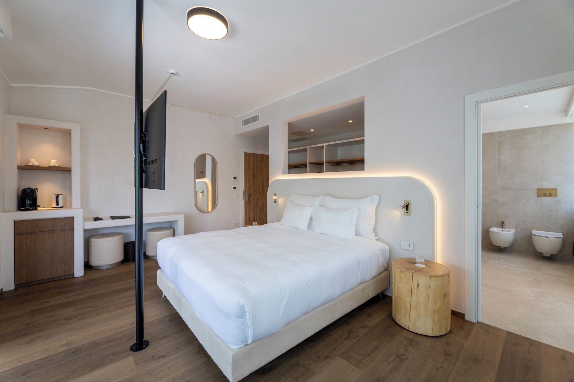 Ein modernes Hotelzimmer mit einem großen Bett, einem kleinen Schreibtisch, einem Spiegel und einem Badezimmer mit Duschwc.