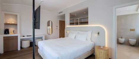 A modern hotel room with a large bed, a small desk, a mirror, and a bathroom with a bidet.