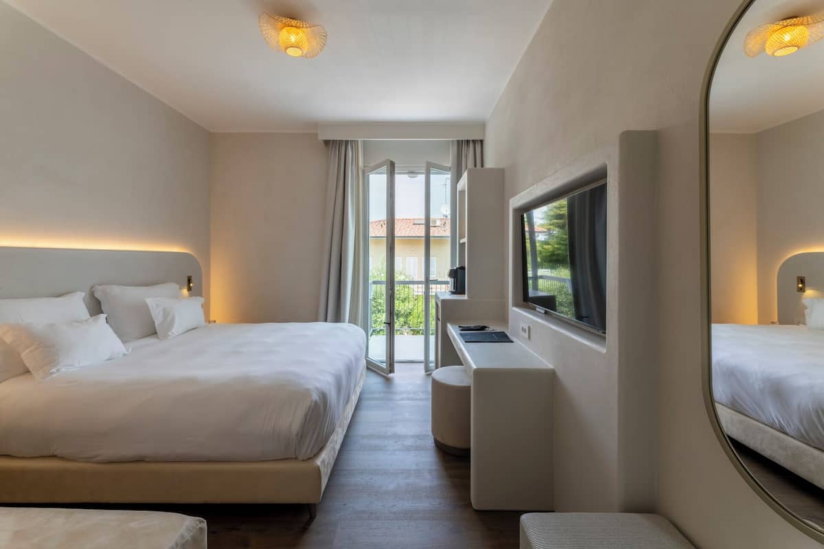A hotel room with two beds, a desk, a TV, and a large mirror.