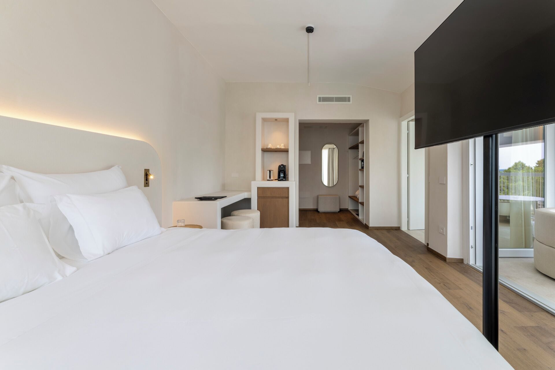 Una habitación de hotel moderna con una cama grande, un escritorio pequeño, un tocador y un balcón con vistas.