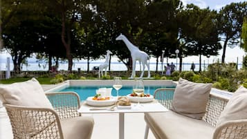 Ein Essbereich mit Korbstühlen und einem Tisch für zwei Personen mit Blick auf einen Pool, im Hintergrund eine Giraffenstatue.
