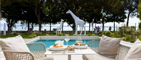 A dining area with wicker chairs and a table set for two, overlooking a pool with a statue of a giraffe in the background.