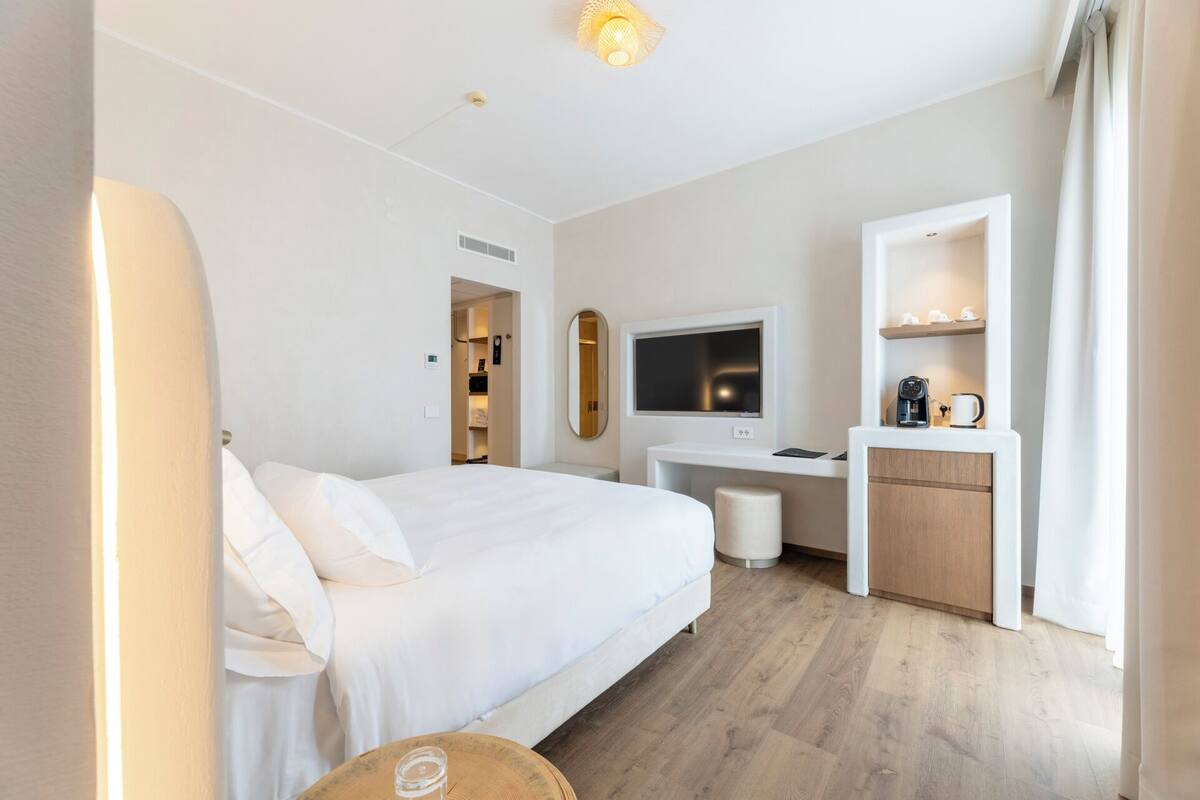 A hotel room with a bed, a desk with a TV, a coffee machine, and a small seating area.