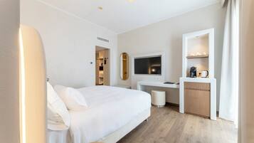 A hotel room with a bed, a desk with a TV, a coffee machine, and a small seating area.