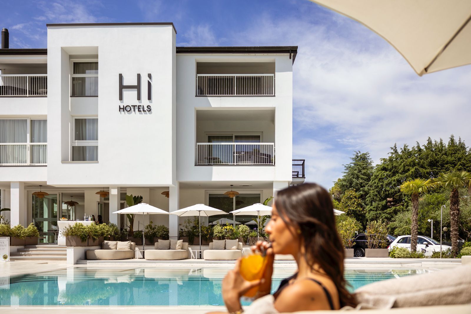 A modern hotel building with a pool area, outdoor seating, and a clear sky.