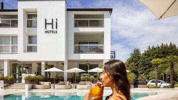 A modern hotel building with a pool area, outdoor seating, and a clear sky.