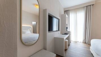 A modern hotel room with a large mirror, a flat-screen TV, a desk, and a comfortable bed.
