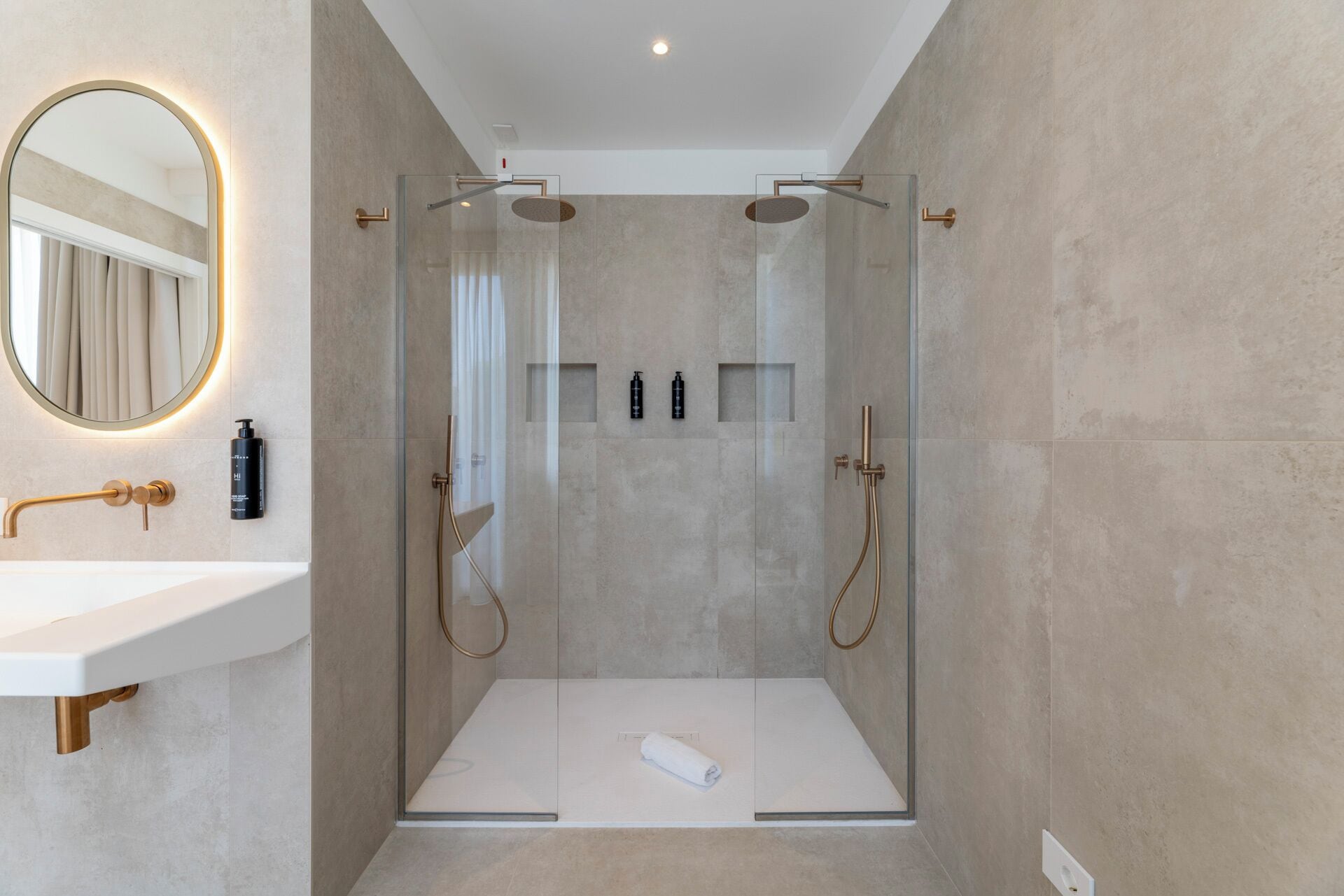 Un baño moderno con ducha envuelta en vidrio, un lavamanos blanco y un espejo redondo con marco iluminado.