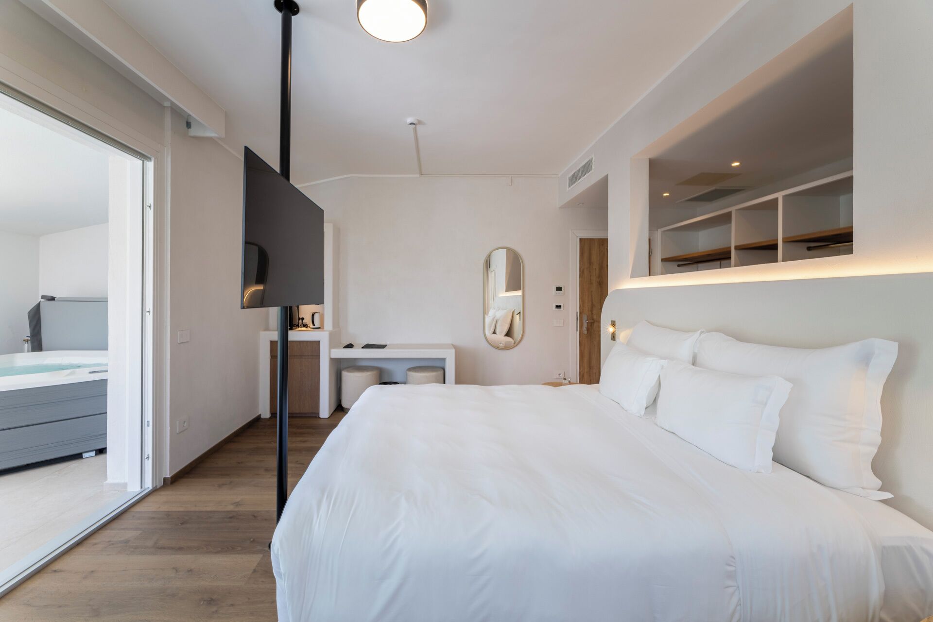 A modern bedroom with a large bed, a desk, and a mirror.