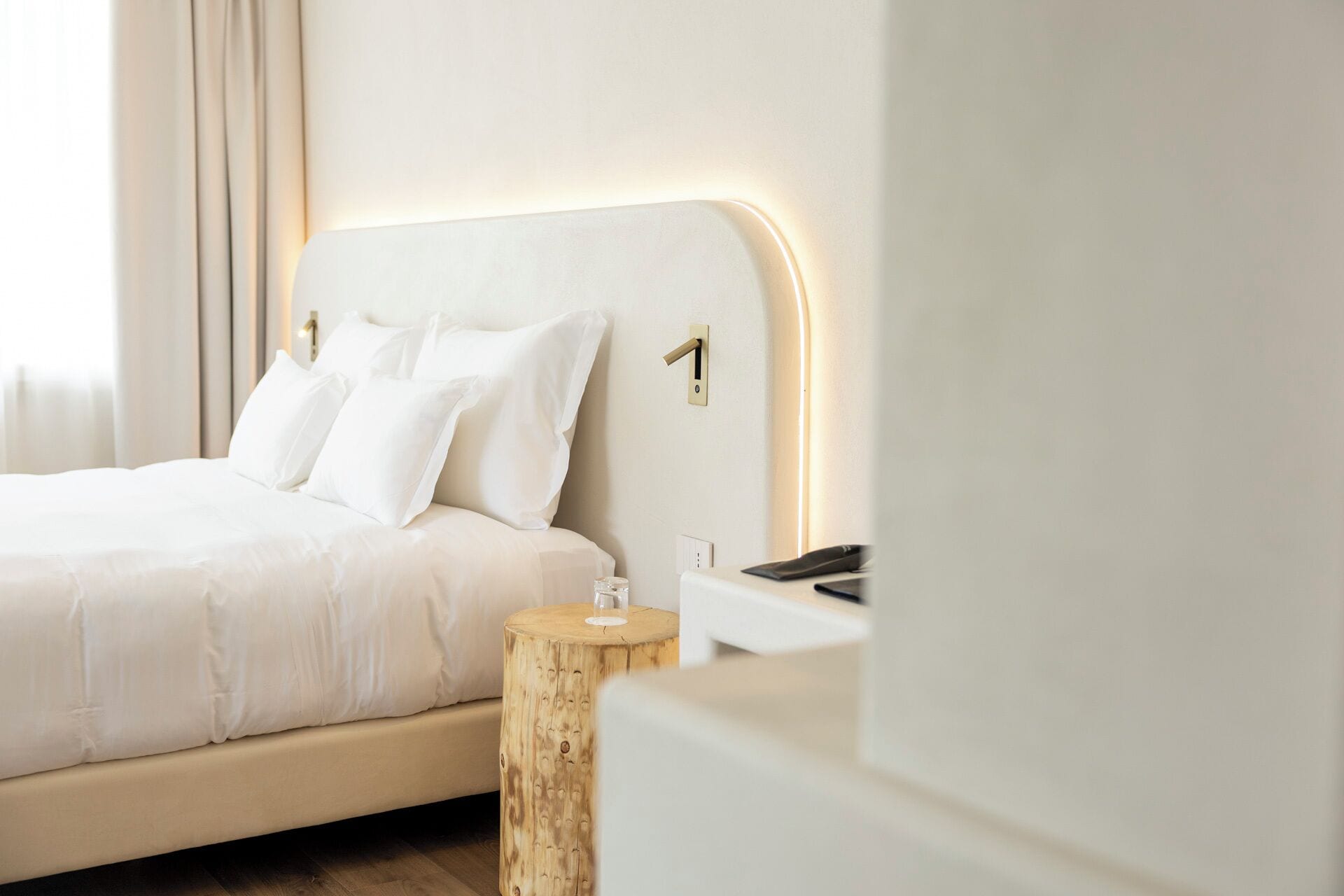 Ein modernes Schlafzimmer mit einem großen Bett, einem Nachttisch mit einem Glas und einem Holznachttisch.