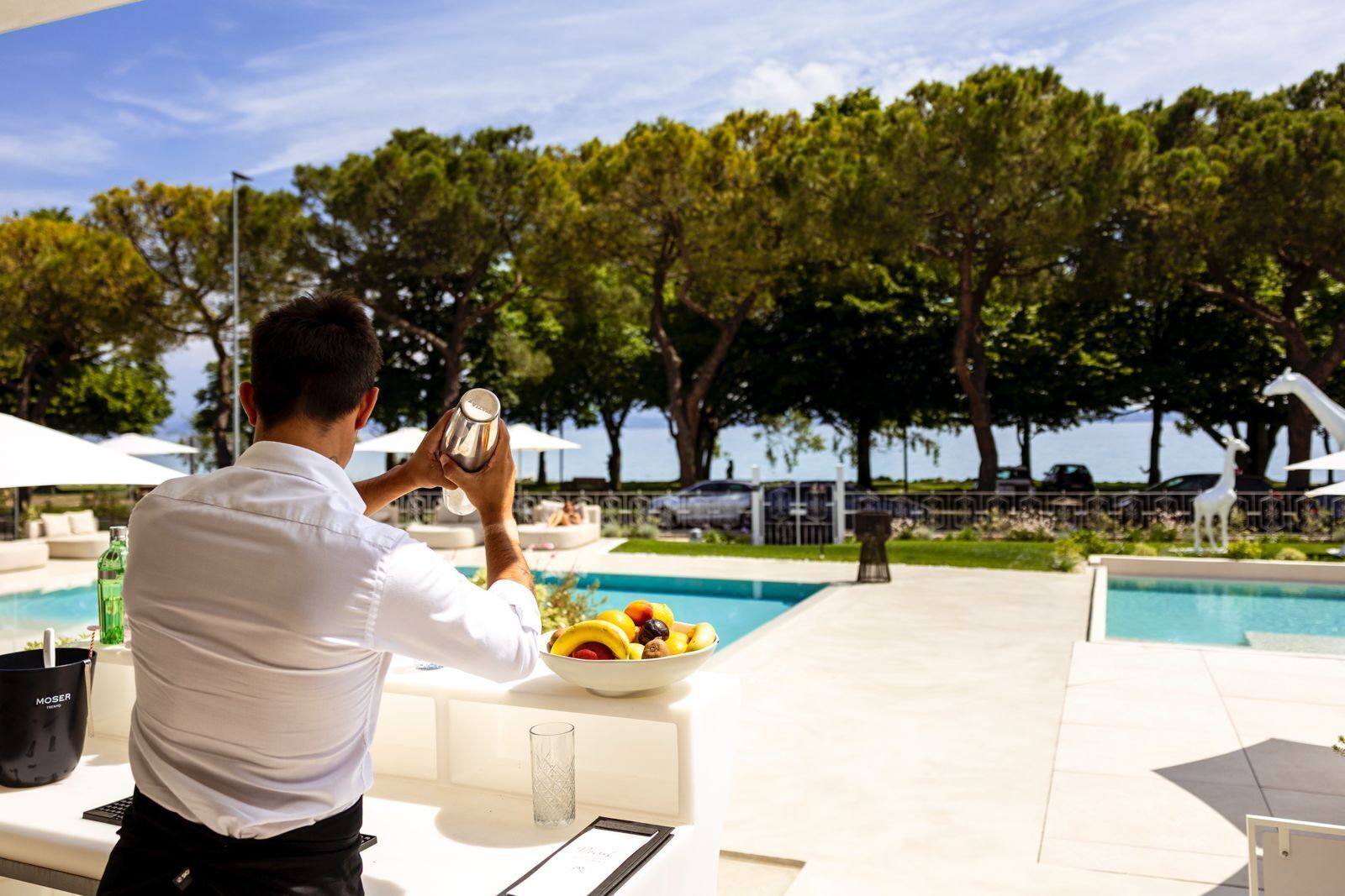 Una persona che scatta una foto con una macchina fotografica, una piscina e un'area pranzo con una ciotola di frutta.