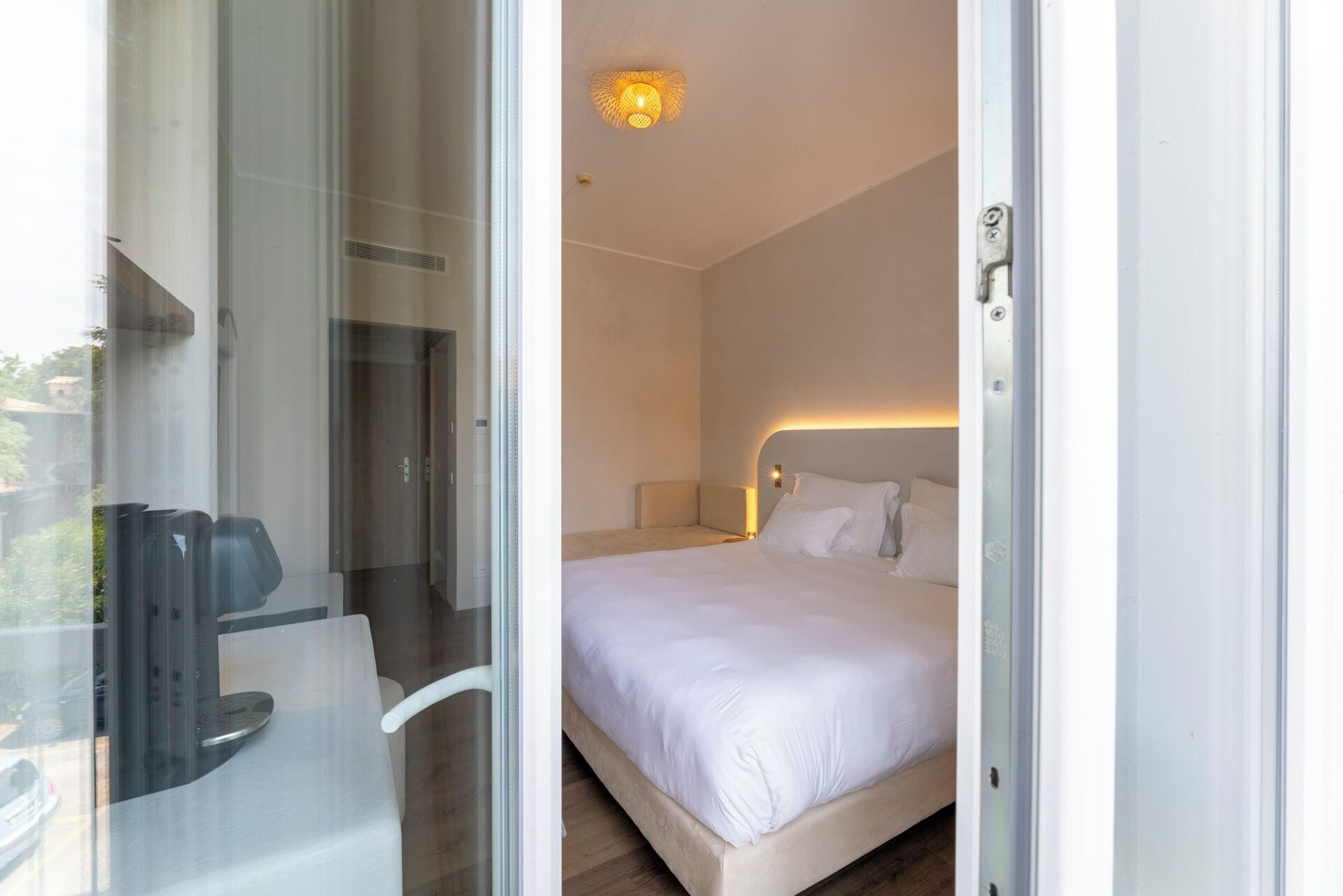 A hotel room with a bed, a chair, a desk, and a glass door leading to an outdoor area.