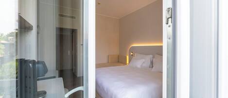 Habitación de hotel con cama, una silla, escritorio y puerta de vidrio que da a un espacio exterior.