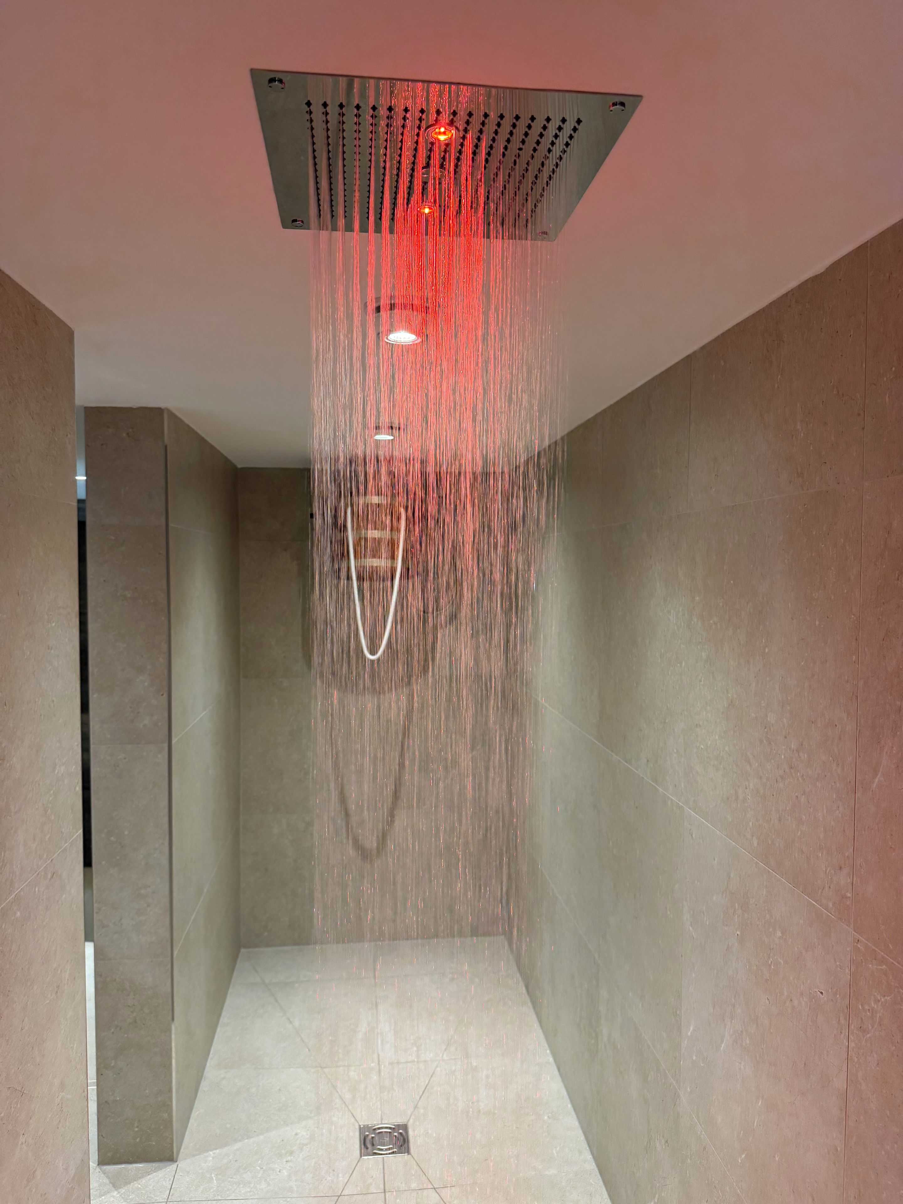 Eine moderne Dusche mit quadratischer Decke, mehreren Düsen und einem sichtbaren Abfluss.