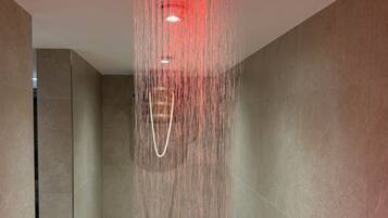Eine moderne Dusche mit quadratischer Decke, mehreren Düsen und einem sichtbaren Abfluss.