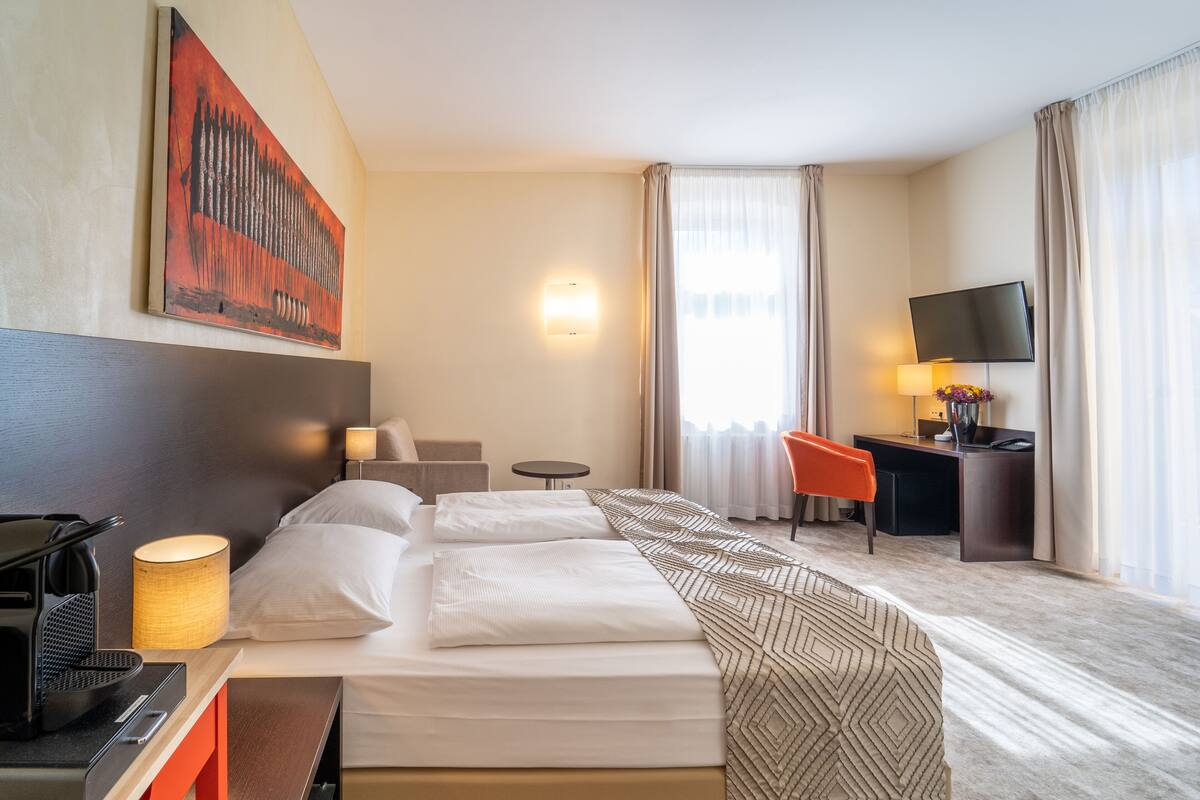 Una camera d'albergo con un letto, una scrivania, una sedia, una televisione e un quadro appeso al muro.