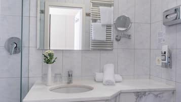 A modern bathroom with a marble sink, a glass shower enclosure, a white vase with flowers, and a towel rack.