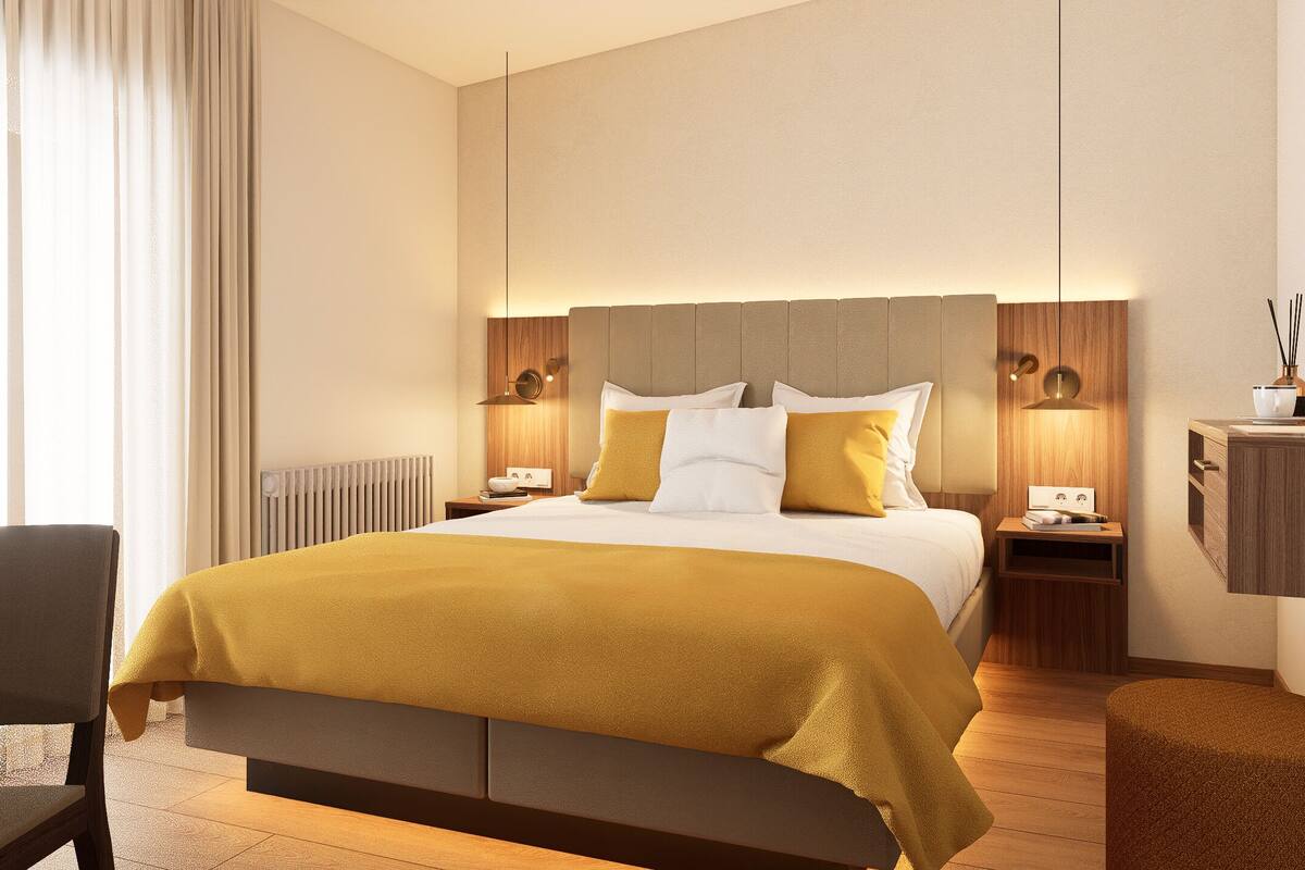 Una camera d'albergo con un letto grande, due comodini con lampade, un tavolino in legno, una sedia e uno sgabello.