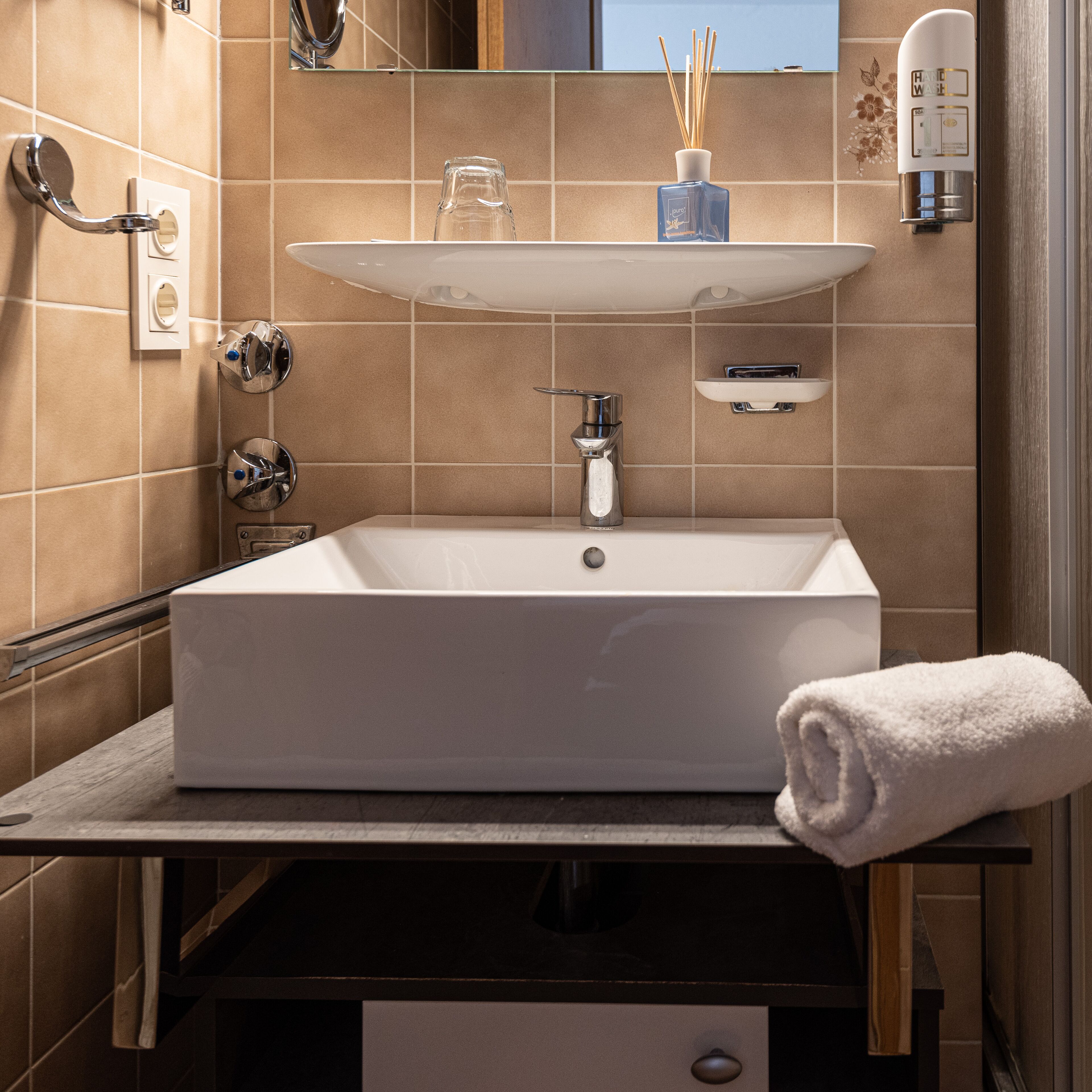 Un baño moderno con un lavamanos rectangular, un frasco de vidrio en la encimera, una toalla y un dispensador de jabón para manos.