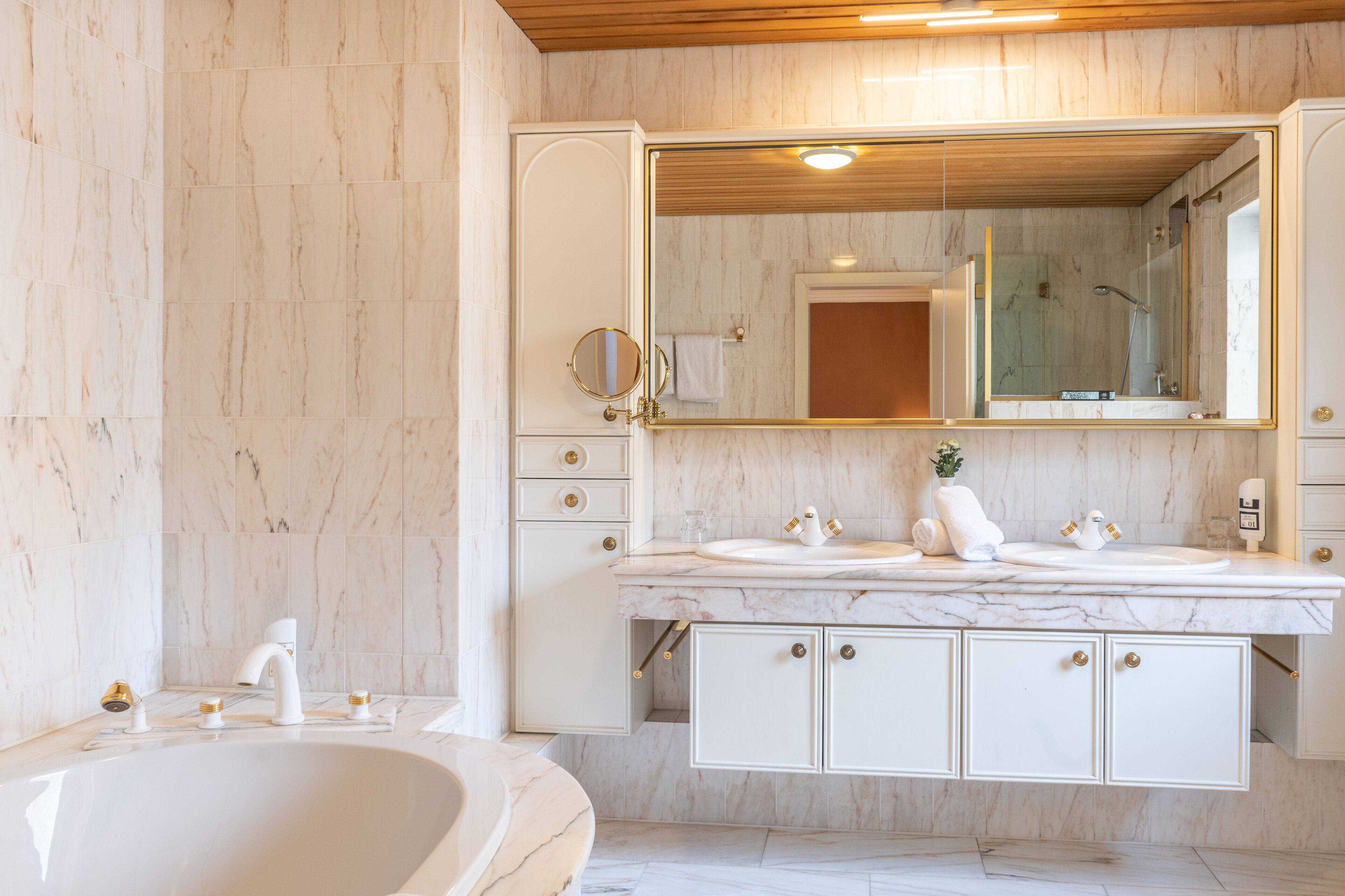 Un baño con una bañera grande, un lavabo doble con pomos dorados y un espejo grande sobre el lavabo.
