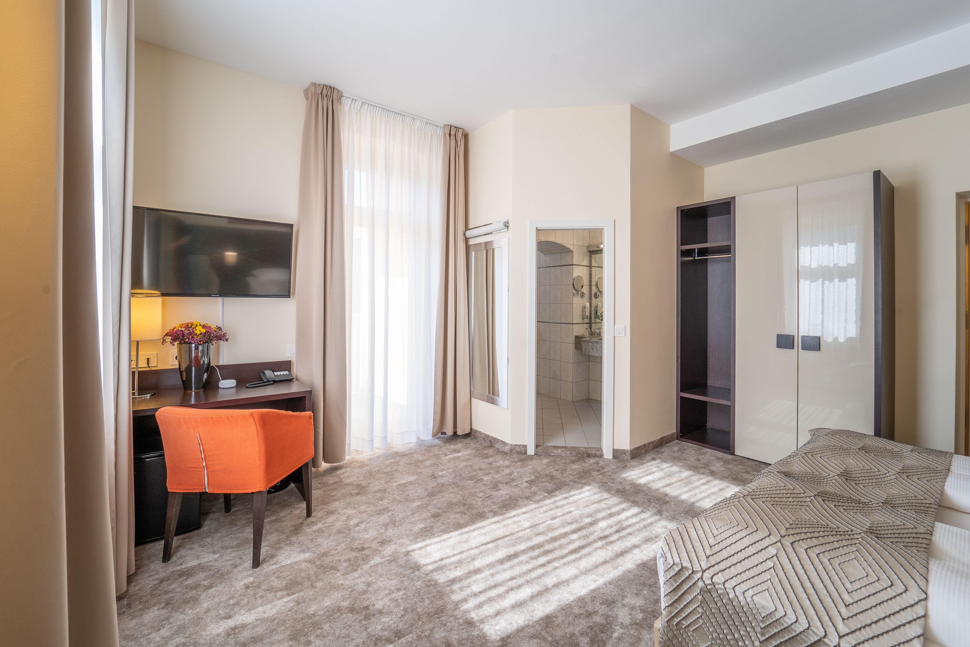 A hotel room with a desk, chair, bed, wardrobe, and a shower area.