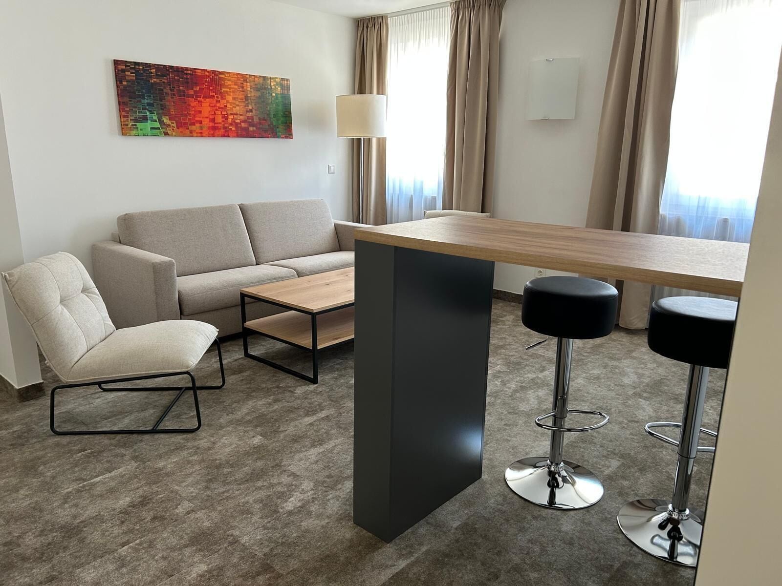 A modern living room with a sofa, a coffee table, a bar area with stools, and a colorful abstract painting on the wall.