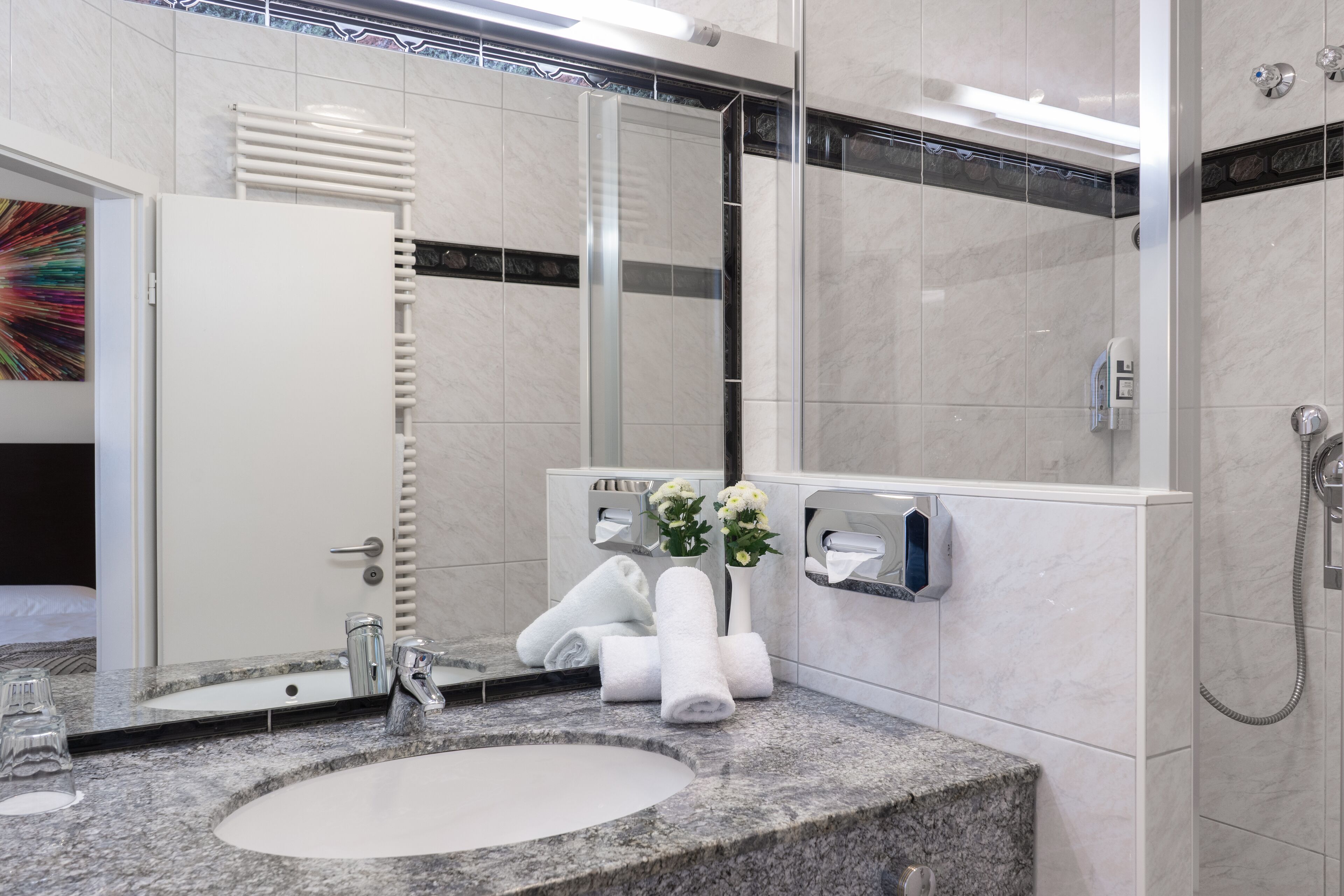 A modern bathroom with a granite sink, a large mirror, a towel rack, and a shower area.
