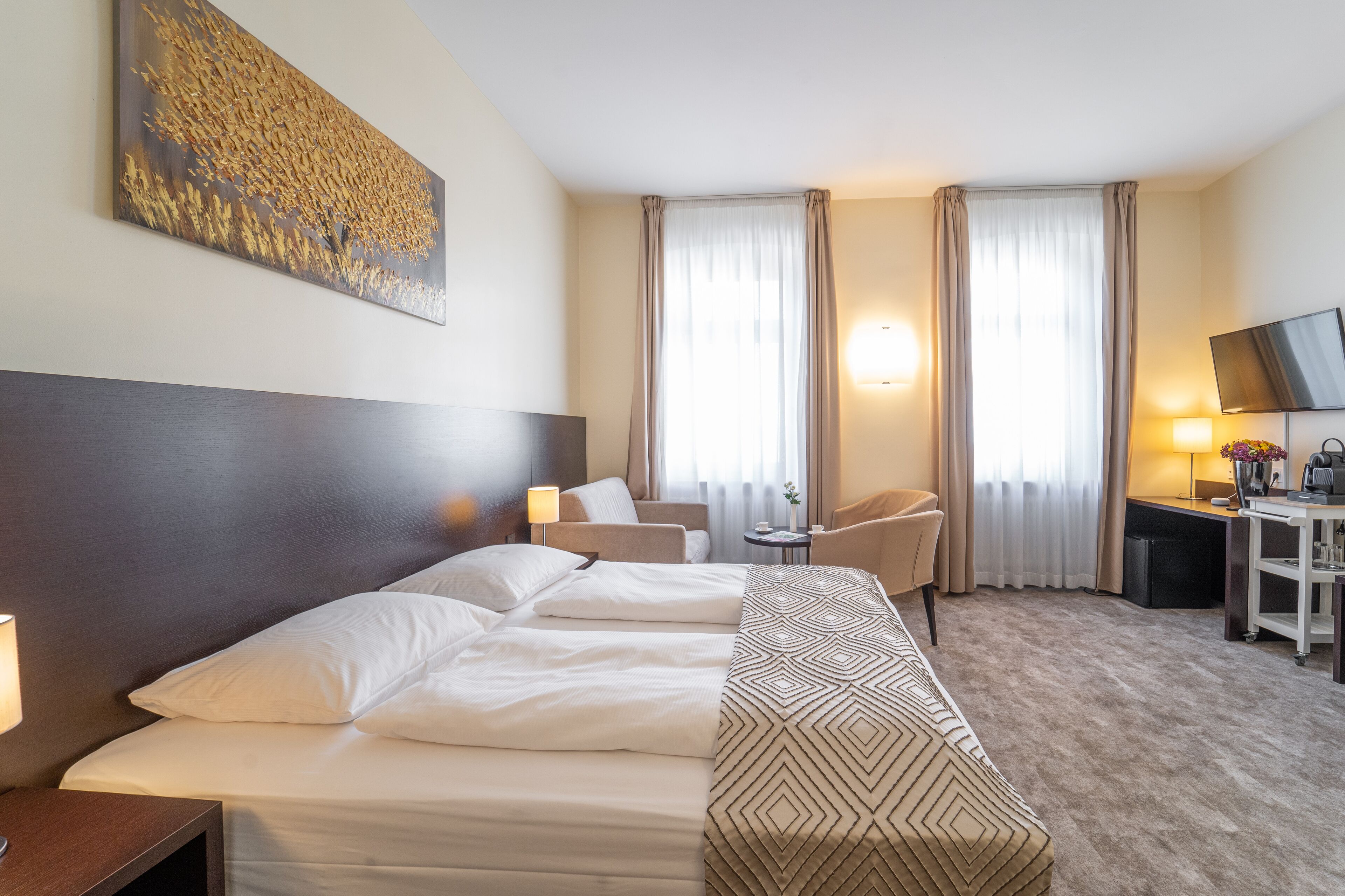 A hotel room with a large bed, two bedside tables, a desk with a chair, a TV, and a painting on the wall.