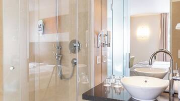 Un baño moderno con ducha de vidrio, lavamanos blanco y un espejo que refleja el ambiente.