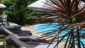 Zona junto a la piscina con sillones, sombrillas y una piscina.