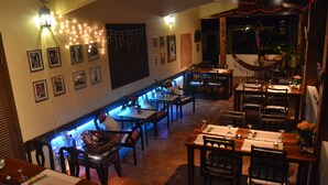 Un restaurante con varias mesas y sillas, luces colgantes y cuadros en las paredes.