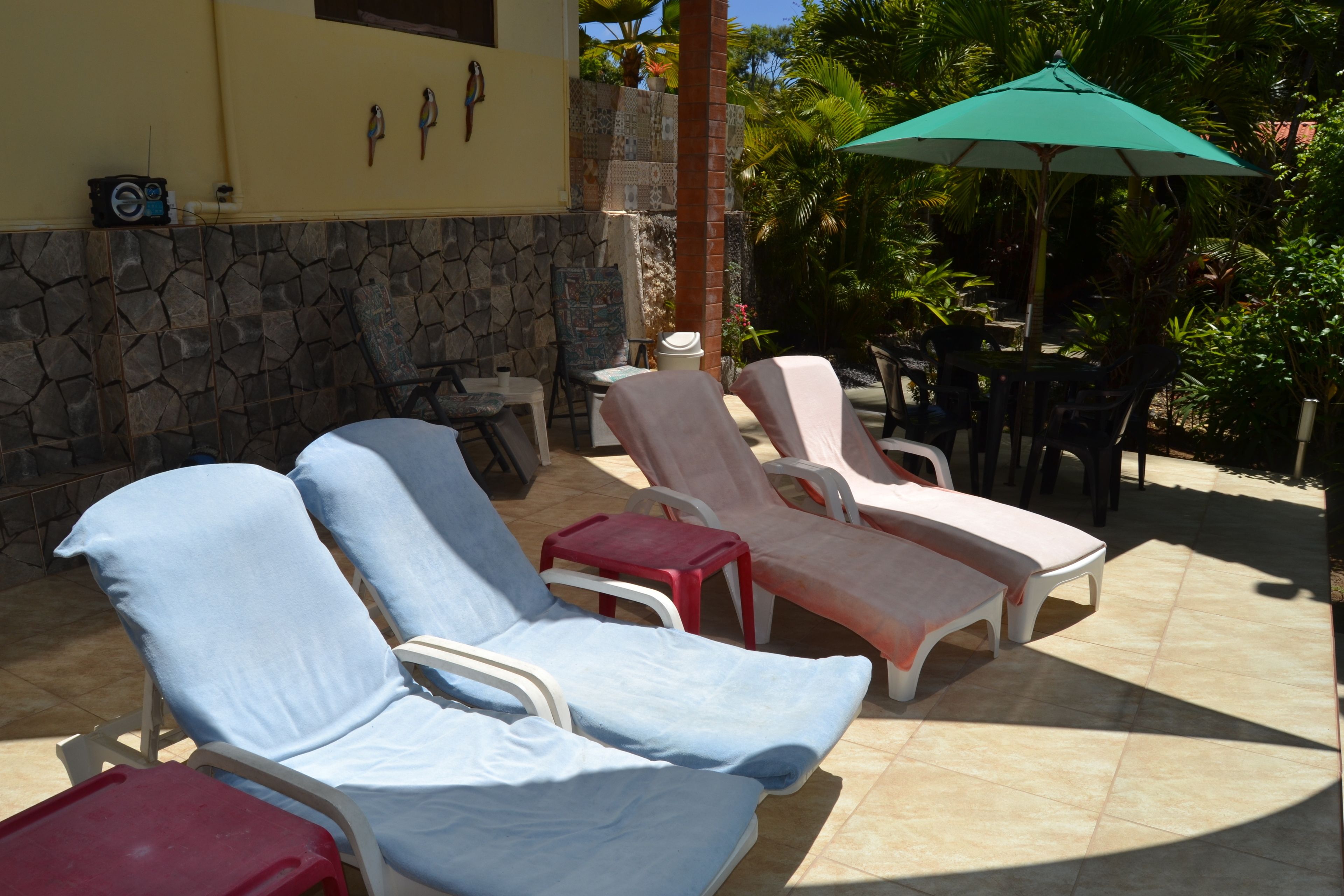 A patio area with lounge chairs and a table, surrounded by a stone wall and plants.
