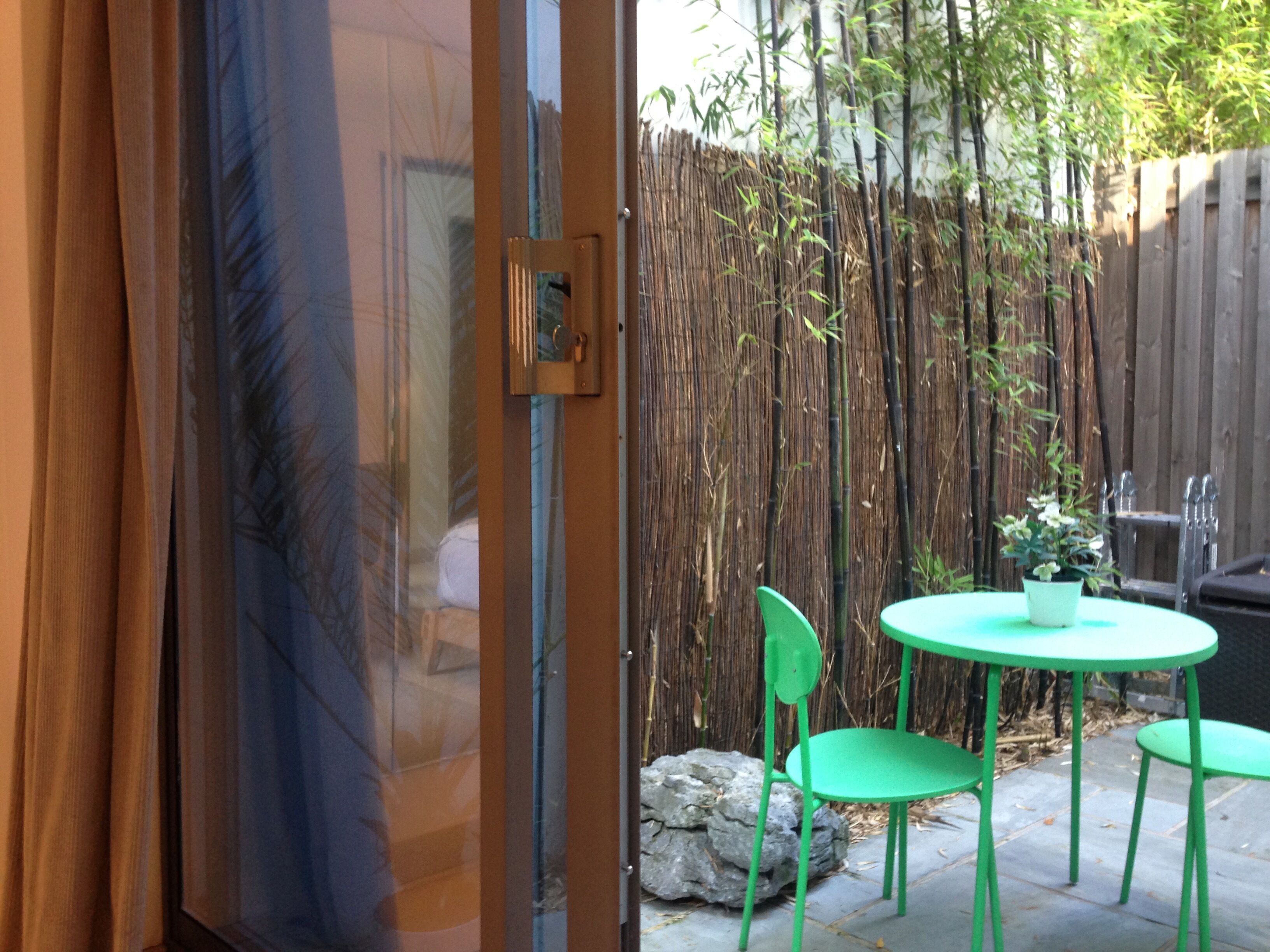 A patio with a glass door, a bamboo fence, and green chairs.