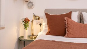 Un dormitorio ordenado con cama, mesita de noche con lámpara, espejo y perchero.