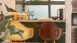 Una cocina moderna con zona de comedor, que cuenta con encimera de mármol, cafetera y un amplio ventanal con vistas a zonas verdes.
