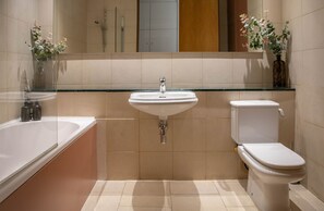 A modern bathroom with a glass-enclosed sink, a white toilet, and a bathtub. - The Luxury Inn (London)
