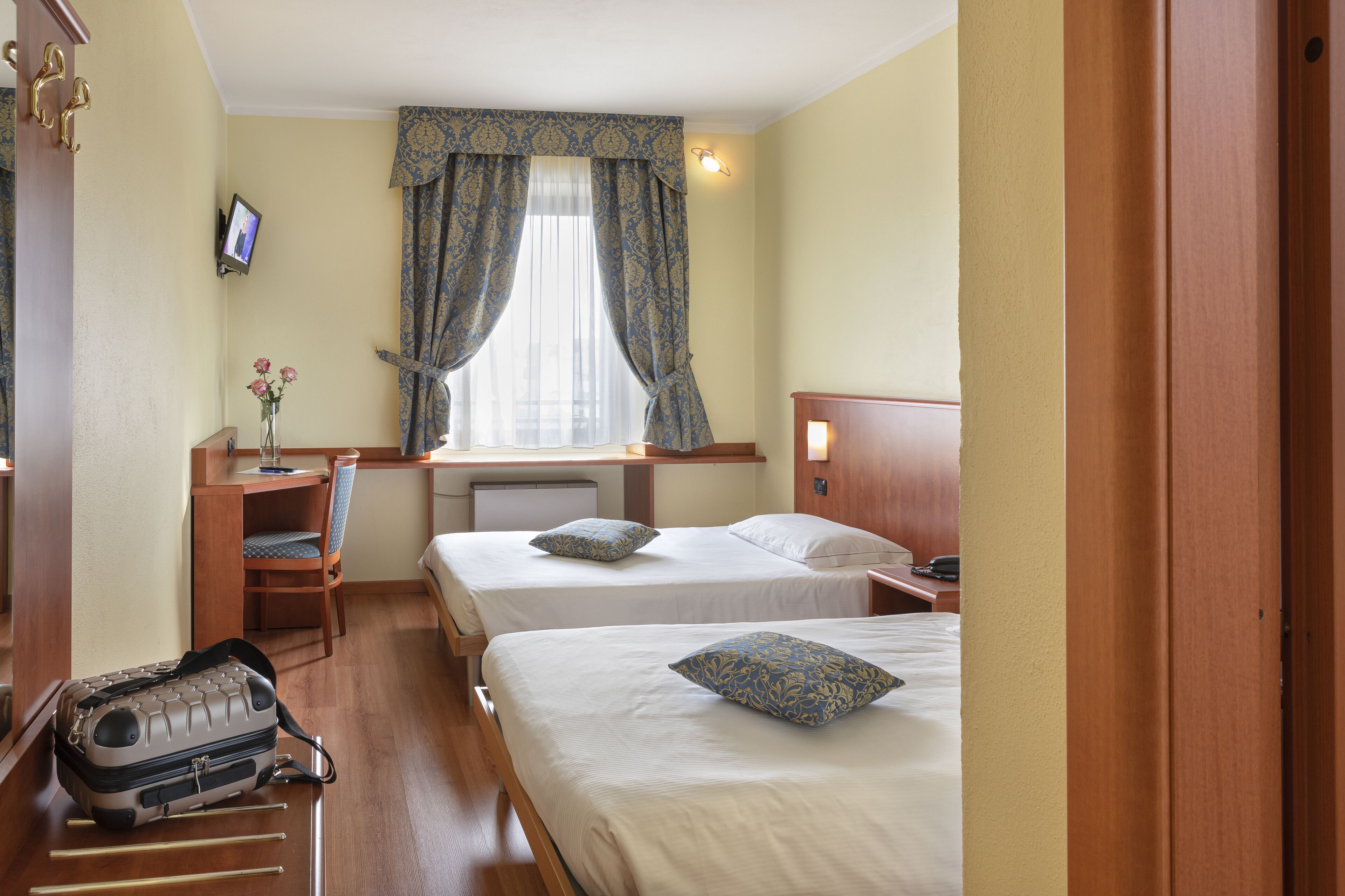 Une chambre d’hôtel avec deux lits, un bureau, une chaise, une télévision et une valise.