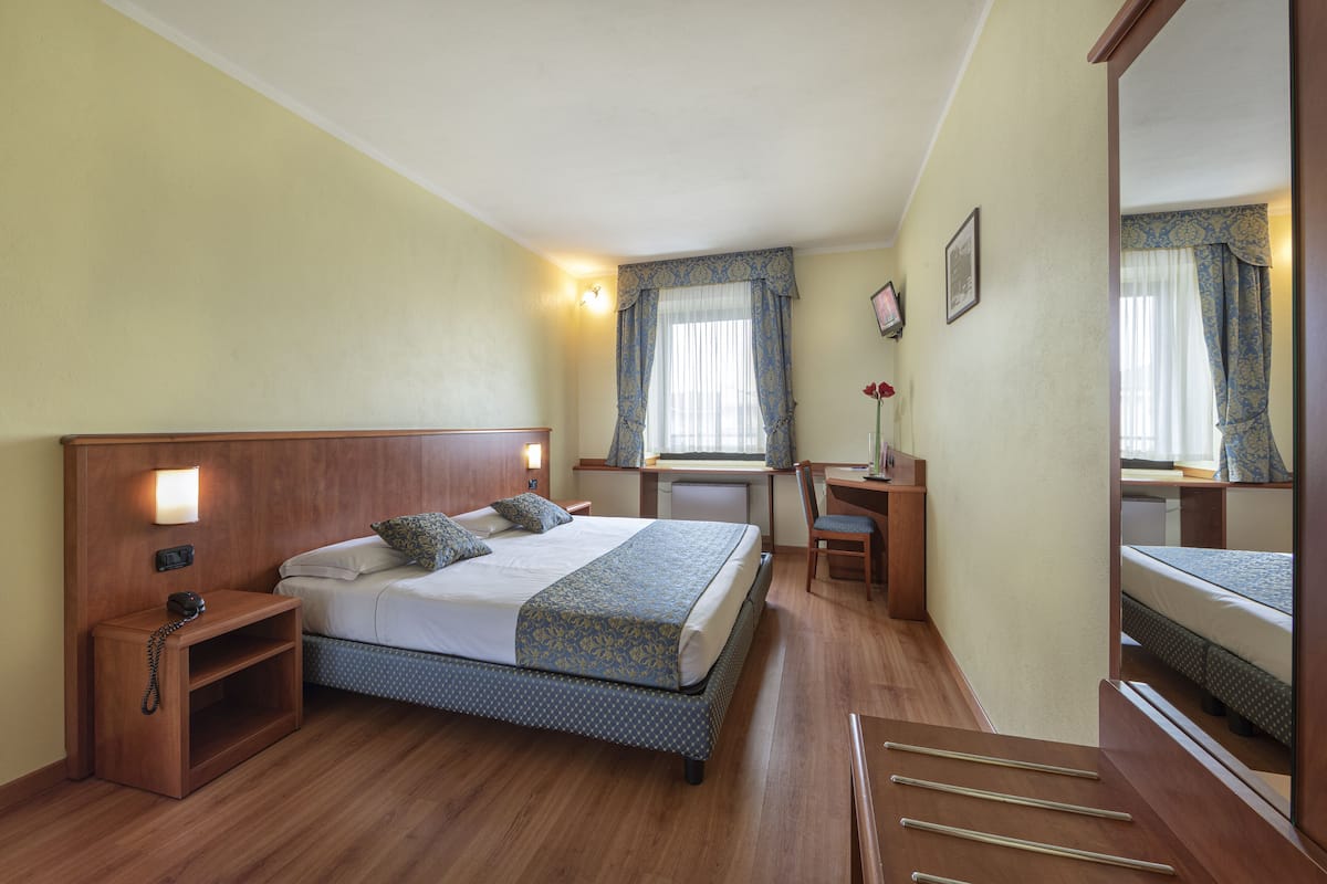 Une chambre d’hôtel avec un lit en bois, des tables de chevet, un bureau et un miroir.