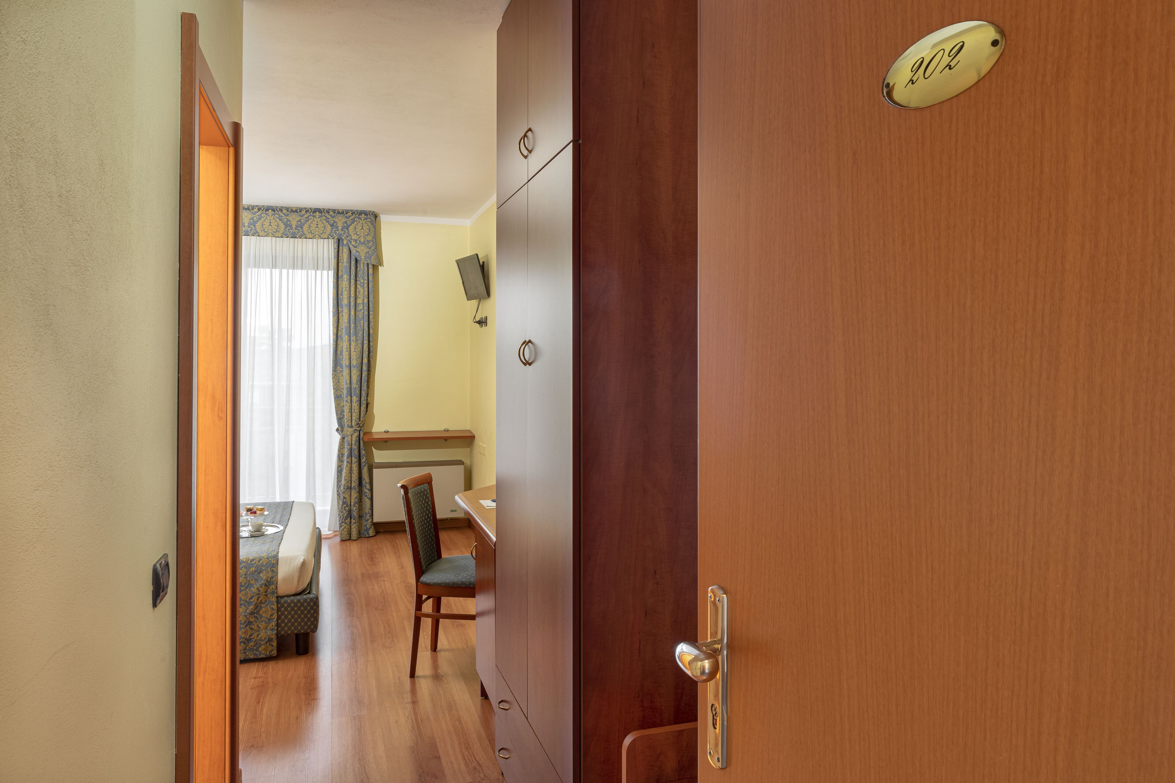 A hotel room with a wooden door, a dining area with a table and chairs, and a visible room number.