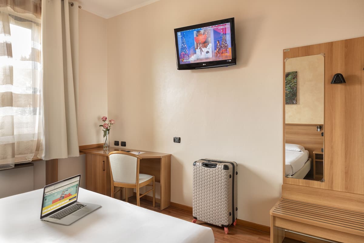 Une chambre d’hôtel avec un lit, un bureau, un ordinateur portable, une télévision et une valise.