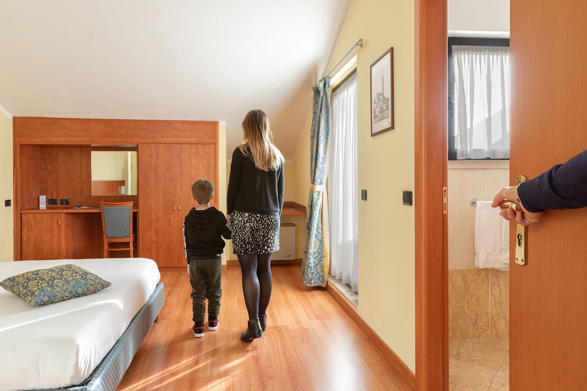 Une chambre d’hôtel avec un lit, un bureau, une chaise et une salle de bain visible à travers une porte ouverte.