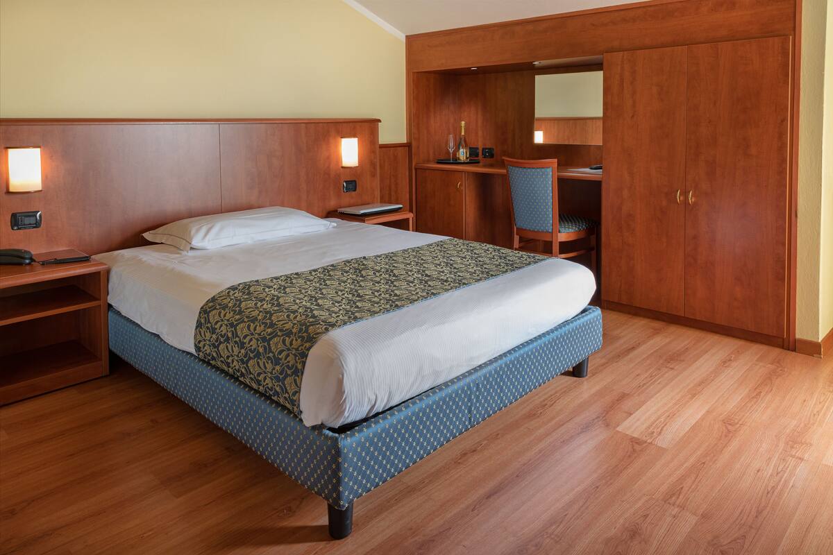 Une chambre d’hôtel avec un grand lit, une tête de lit en bois, des tables de chevet, un bureau, une chaise et une armoire.