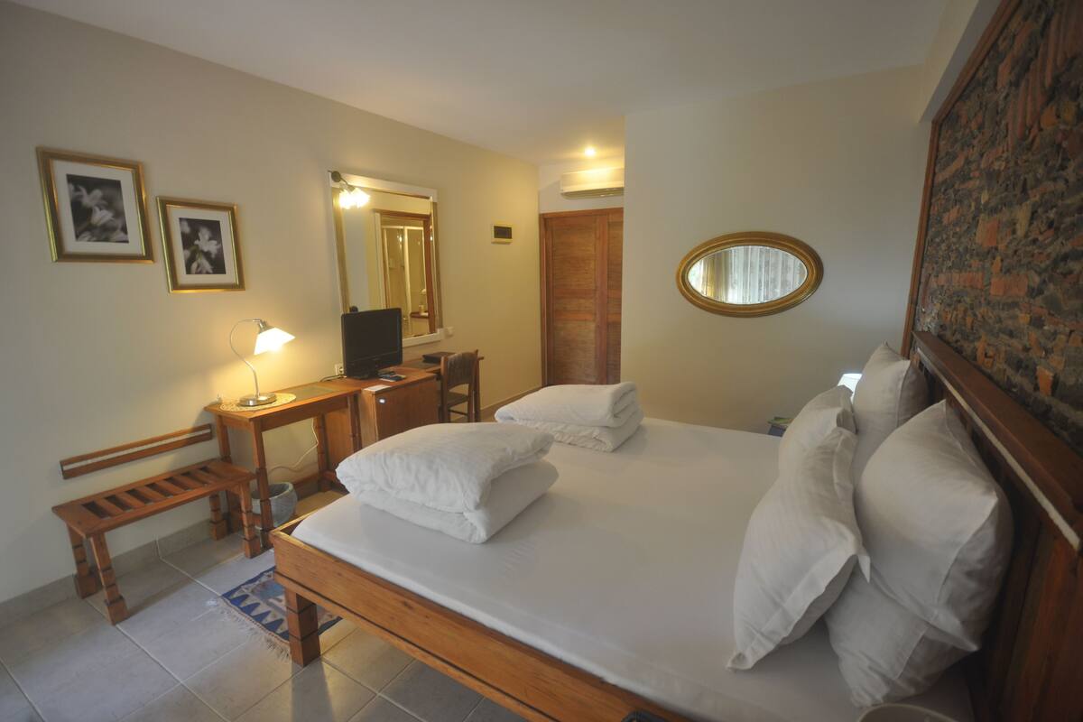 A neatly arranged bedroom with a bed, bedside tables, a desk, a chair, a bench, a mirror, and a wall-mounted picture frame.