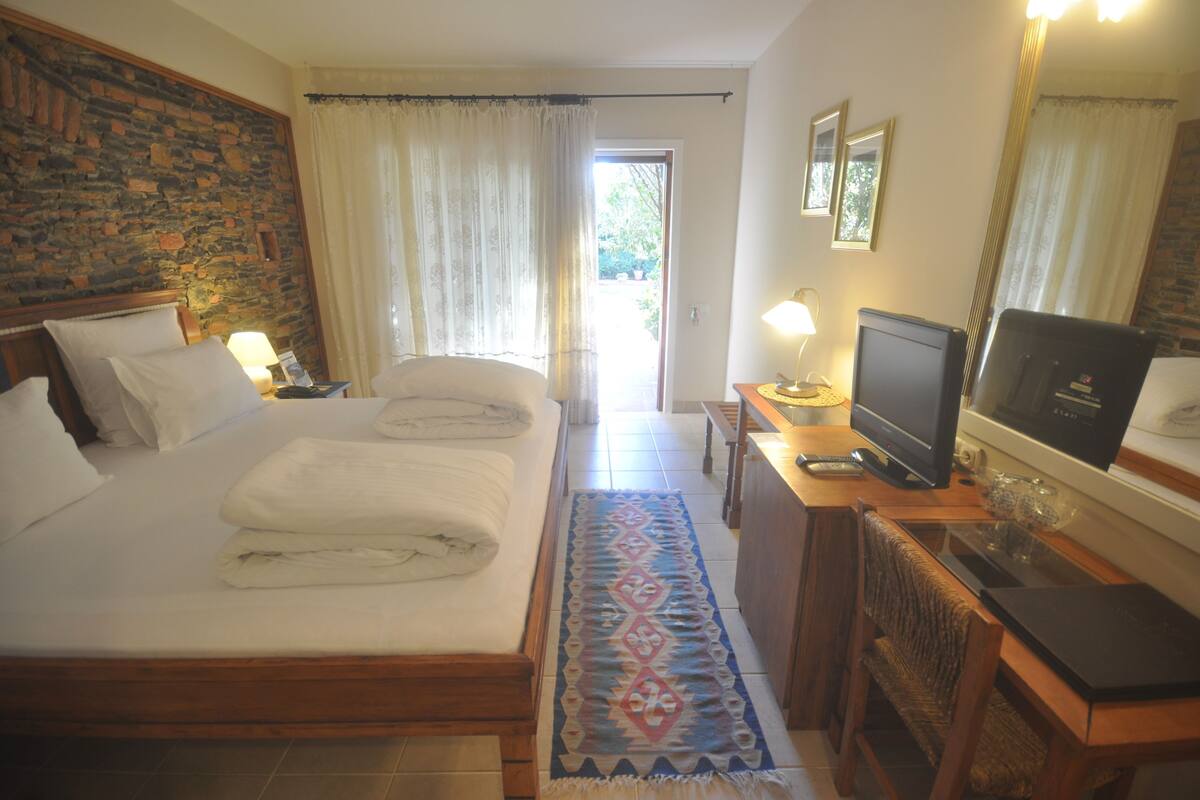 A hotel room with a bed, a desk with a television, a mirror, and a window with curtains.