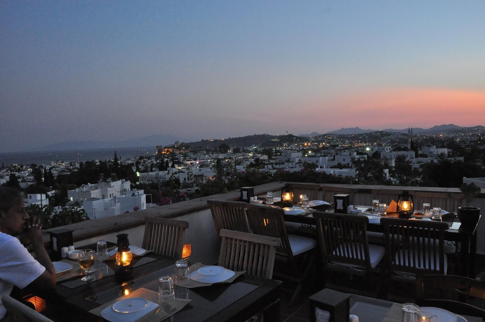 Un espace de restauration aménagé sur le toit, avec des tables pour deux, offrant une vue sur le paysage urbain au crépuscule.