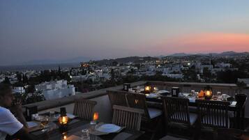 Un espace de restauration aménagé sur le toit, avec des tables pour deux, offrant une vue sur le paysage urbain au crépuscule.