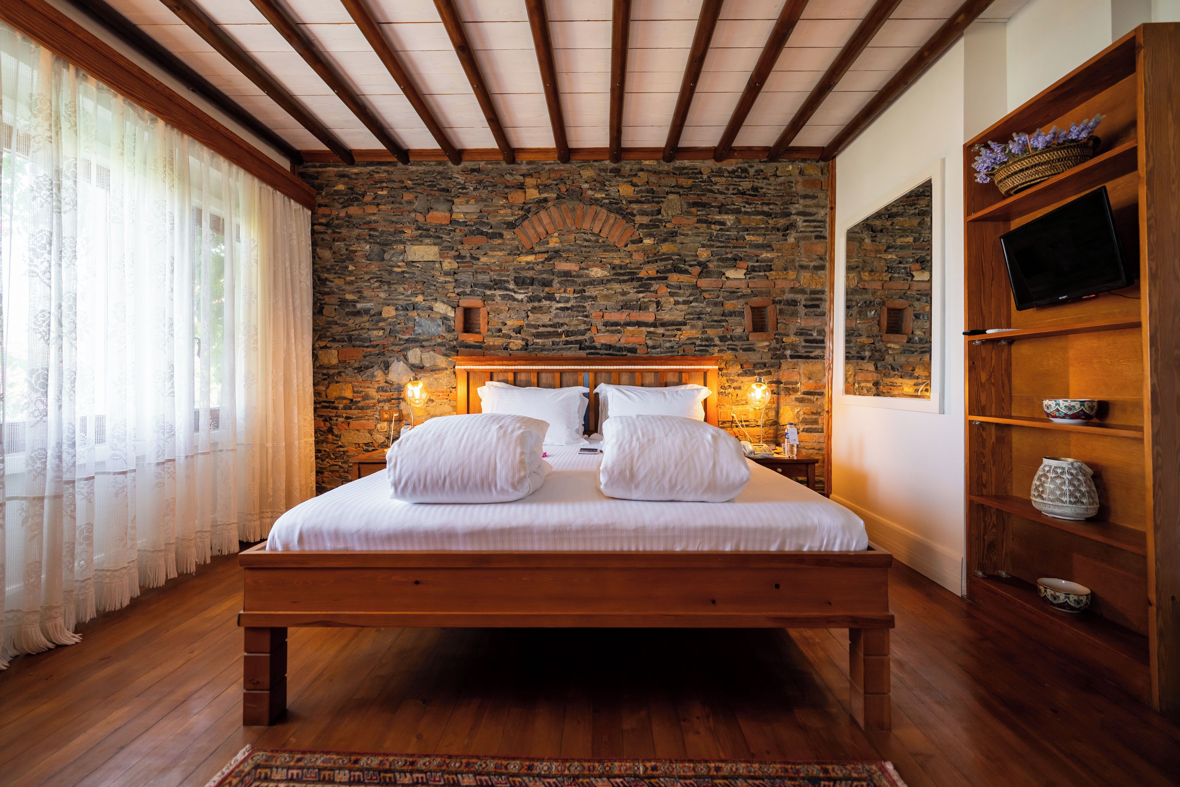 A bedroom with a stone wall, wooden bed frame, and a television on a wooden shelf.