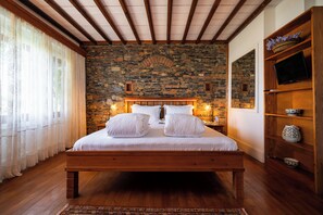 A bedroom with a stone wall, wooden bed frame, and a television on a wooden shelf. - El Vino Hotel Suites - Special Class (Bodrum)