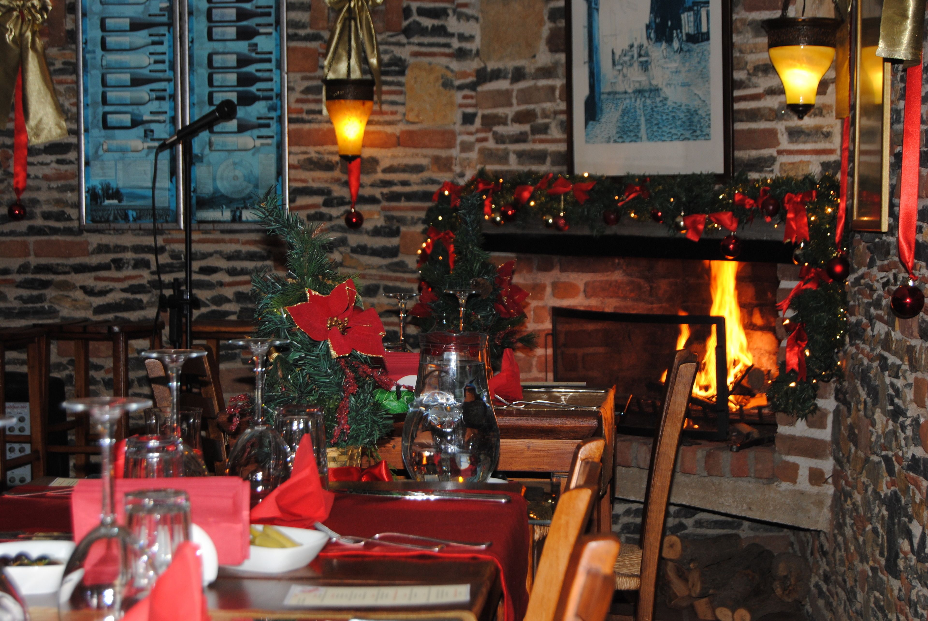A warmly lit dining area with a fireplace, wooden furniture, and festive decorations.